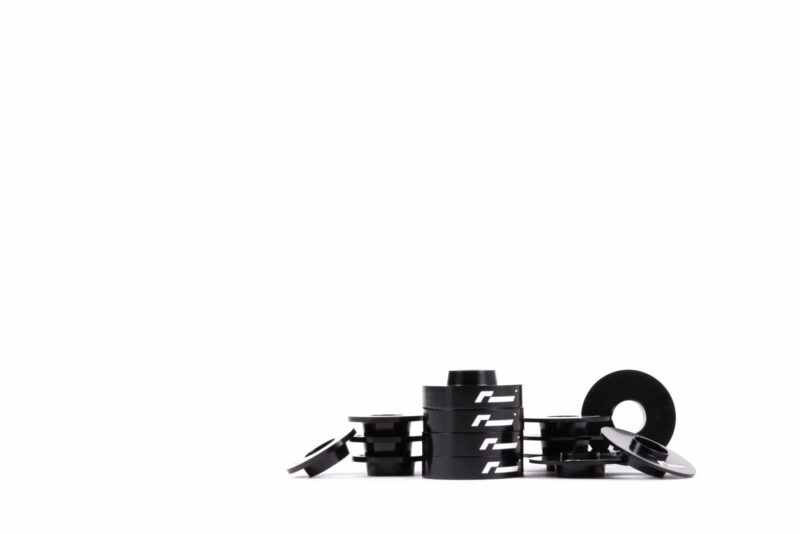 dead-set-4_45145483134_o-scaled-2jpg - OPSHOLDERS Close-up of black interlocking bricks with white logos arranged in a circular stack on a white background.