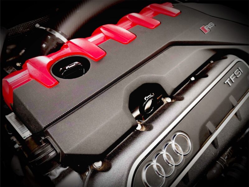 dipstick_5jpg - OPSHOLDERS Close-up of an Audi engine cover with red intake fins and the TFSI badge, four-ring logo visible.