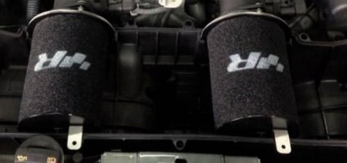 filtre-a-air-racingline-audi-r8-52-v10__604791490375847-1jpeg - OPSHOLDERS Two cylindrical black foam air filters with white branding mounted in a car engine bay.