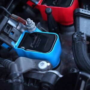 Close-up of a car battery terminal: blue terminal cover with a red jumper cable attached to a metal post under the hood.