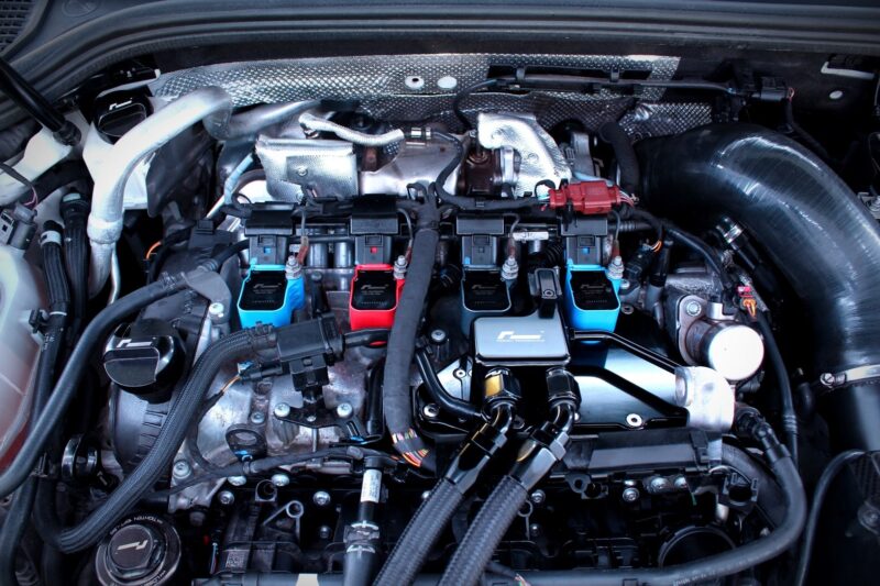 Close-up of a car engine bay with blue and red aftermarket coil packs and wiring harnesses