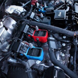 Engine bay with assorted electronic diagnostic modules (red, blue) plugged into wiring harnesses amid hoses and metal components.