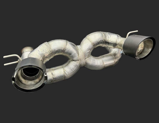 maserati-mc20-2020-exhaust-stage1-seletronjpg - OPSHOLDERS Twin exhaust pipes with braided, heat-wrapped center section on a dark background; after-market exhaust component.