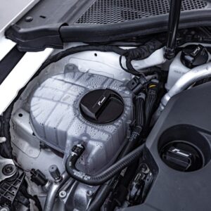 oil-cap-gen4-mqb-evo_51745577247_o-1jpg - OPSHOLDERS Close-up of a car engine bay showing the translucent coolant reservoir with a black cap and surrounding hoses and components.