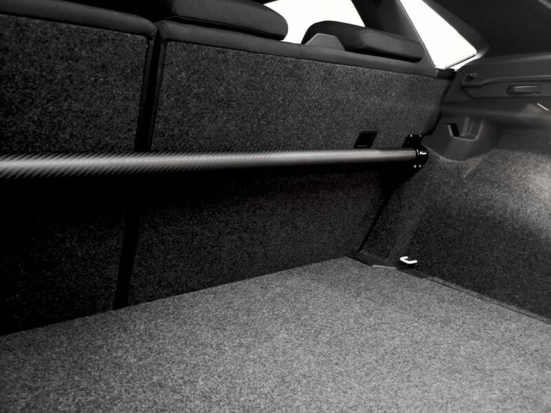 Car trunk interior with folded rear seats and a long cylindrical rod along the carpeted floor (black and white).