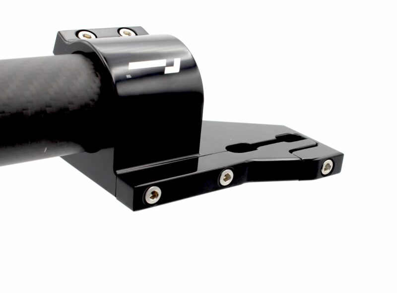 Close-up of a glossy black camera tripod quick-release plate with two exposed screws on top and a carbon‑fiber-like grip arriving from the left.
