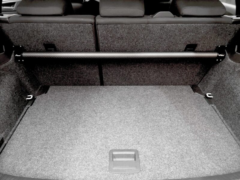 Rear cargo area of a car with a long black carbon‑fiber crossbar spanning the space behind the folded rear seats.