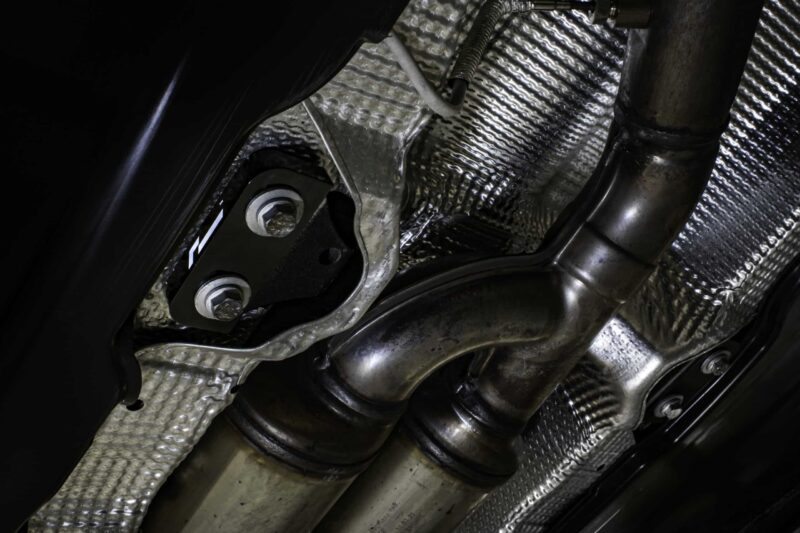 propshaft-bearing-alignment-kit_51769411775_o-scaled-2jpg - OPSHOLDERS Close-up of a vehicle’s exhaust pipe and mounting bracket with heat shielding and braided insulation visible underneath.