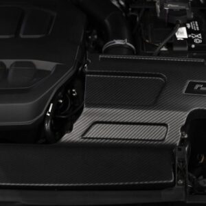 Close-up of a car engine bay with carbon-fiber panels and a visible battery on the right side.