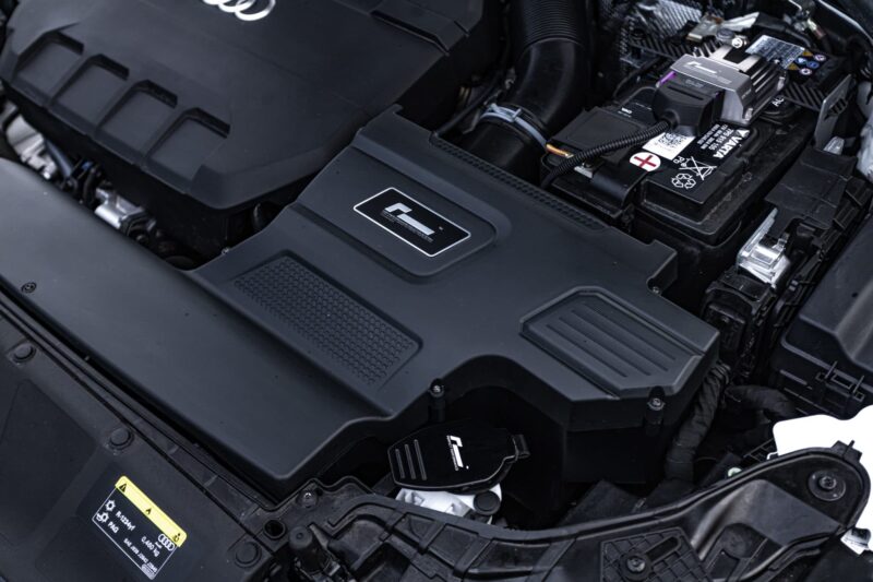 r600-evo_51818344591_o-scaled-2jpg - OPSHOLDERS Close-up of a car's engine bay highlighting the battery and surrounding plastic covers.