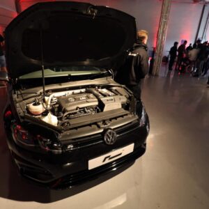 Black VW car with hood open on display at an indoor event, engine visible and people standing in the background.