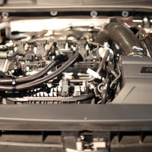 Car engine bay with hoses, wiring, and a large air intake on the right under the hood of a car