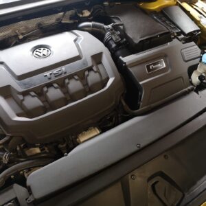 Engine bay of a Volkswagen with a prominent TSI engine cover and VW emblem, showing air intake hose and surrounding components.