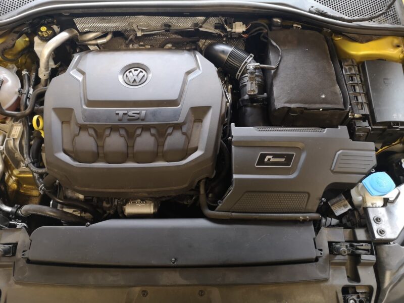 Volkswagen engine bay with a prominent TSI cover and air intake hose on the right side.