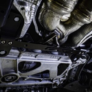 racingline-front-subframe-brace-9_51826108513_o-scaled-2jpg - OPSHOLDERS Underside of a vehicle showing exhaust pipes, heat shields, and metal chassis in a dimly lit area.