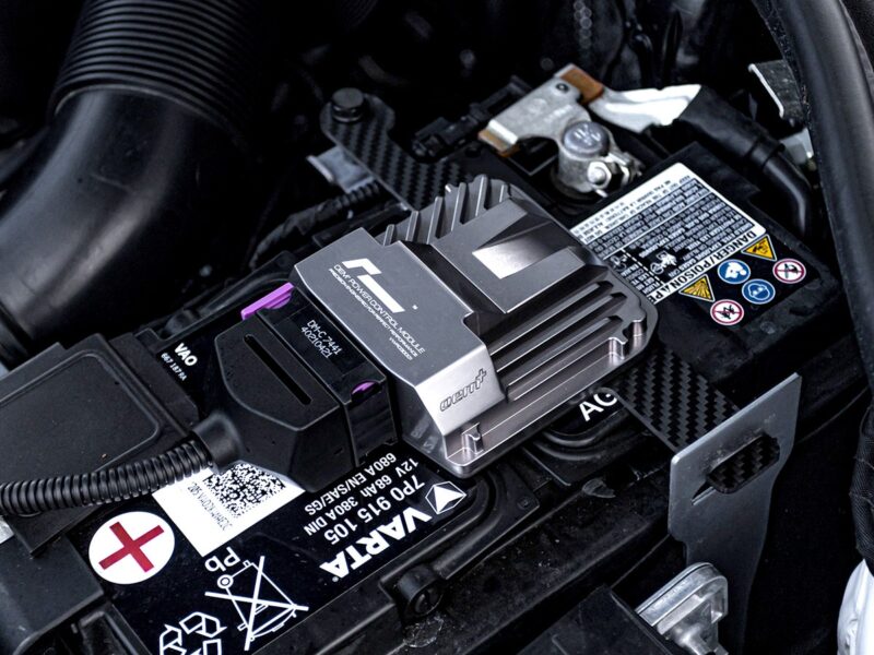Car battery with a metal heatsink/module attached to the top, likely a performance electronic control unit on the terminal area