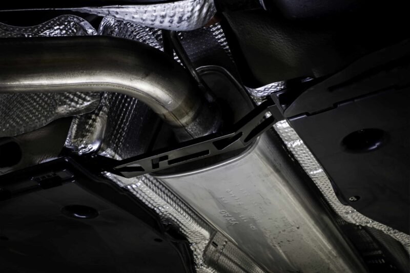Close-up of a vehicle’s undercarriage showing metallic heat shields and dark chassis components nearby.