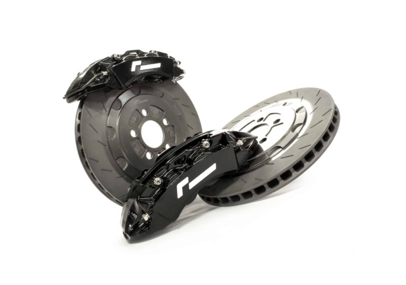 stage-2-evo-brake-kit_51479161930_o-scaled-2jpg - OPSHOLDERS Close-up of a black disc brake caliper mounted on a perforated metal brake rotor against a white background.