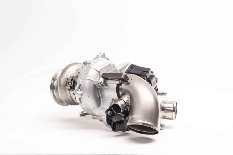 Close-up of a silver industrial turbine or exhaust component with ducts and connectors on a white background.