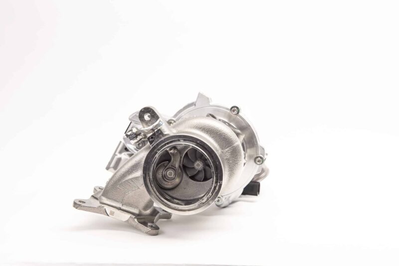 Close-up of a metallic automotive turbocharger housing with visible turbine blades and mounting flanges against a white background