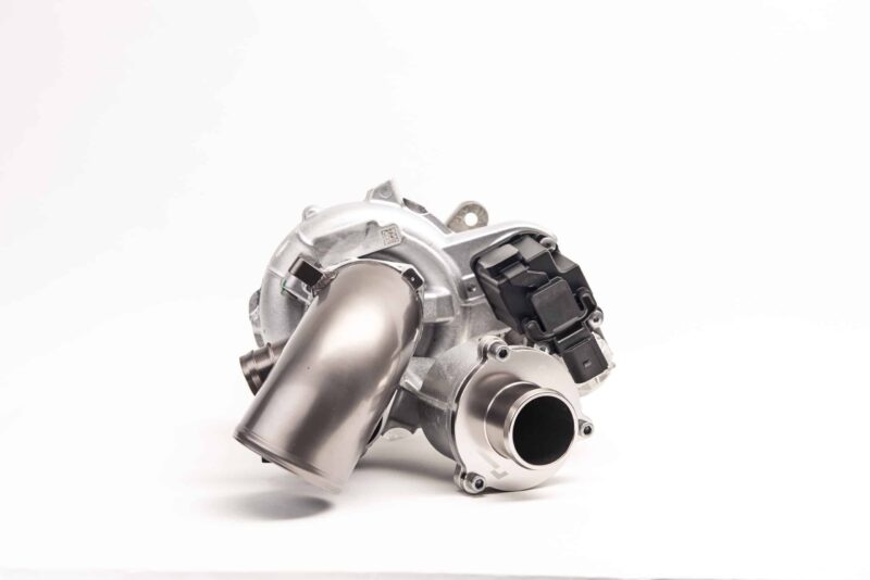 Close-up of a silver automotive engine component against a white background, showing bolts and black connectors.