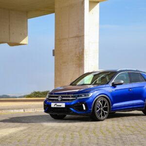 vw-t-roc-r-sport-springs_52959778579_ojpg - OPSHOLDERS Blue Volkswagen SUV parked on a paved lot beside large concrete columns with a clear sky behind.