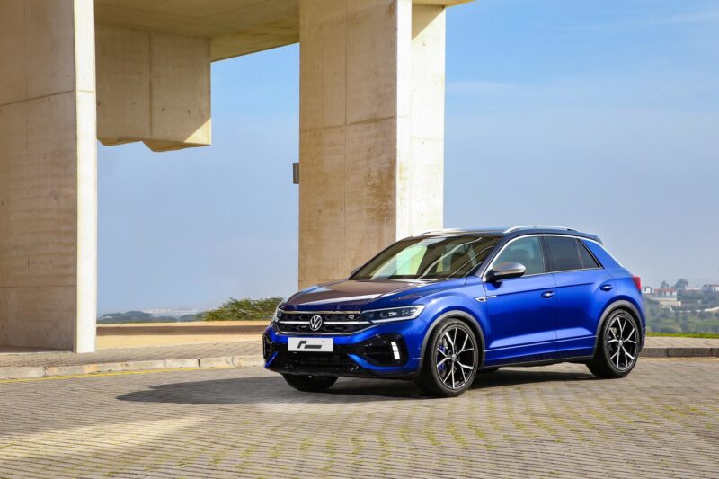 vw-t-roc-r-sport-springs_52959778579_ojpg - OPSHOLDERS Blue Volkswagen SUV parked on a paved lot beside large concrete columns with a clear sky behind.