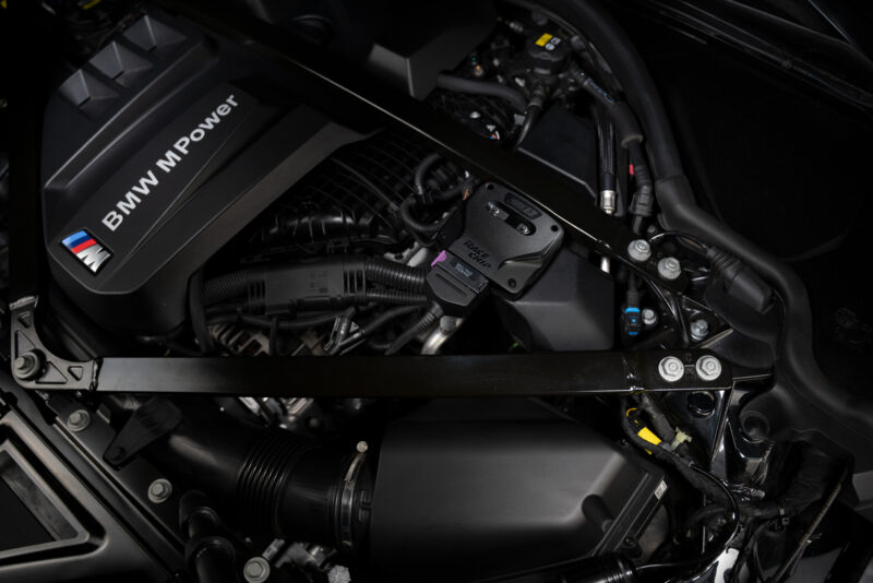 DSC02599 - OPSHOLDERS BMW engine bay with a black engine cover labeled 'BMW M Power' and surrounding hoses and components.