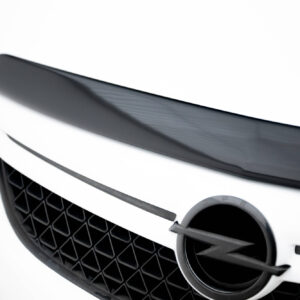 Close-up of a white car front showing a large circular emblem and the grille behind it, with a wiper resting across the area.