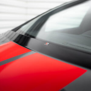 Close-up of a red car hood with a bold black stripe running along it and a blurred windshield in the background.