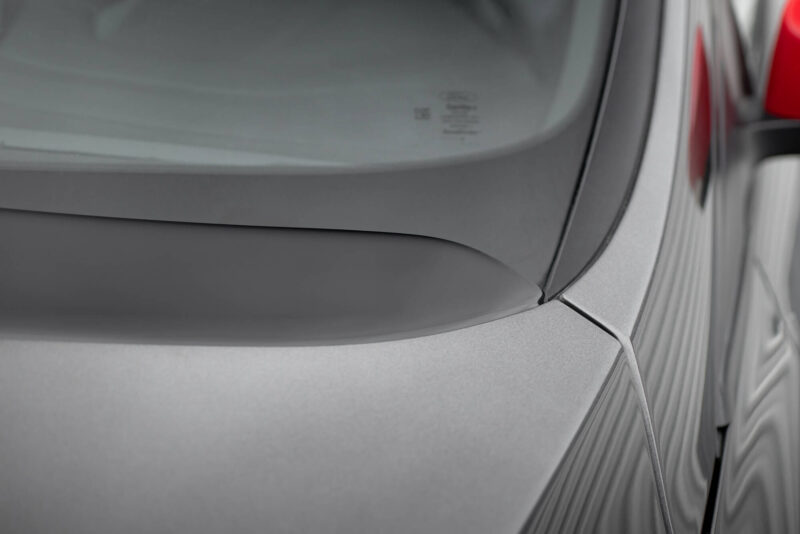 Close-up of a silver car's rear window and trunk area, with a thin cord running along the edge.