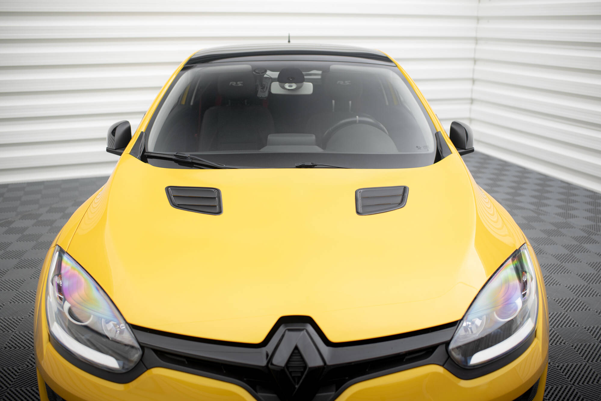 pol_po_Bonnet-Vents-459_2jpg - OPSHOLDERS Front view of a bright yellow car with a black grille, shown indoors on a checkered floor with a sleek hood and headlights visible