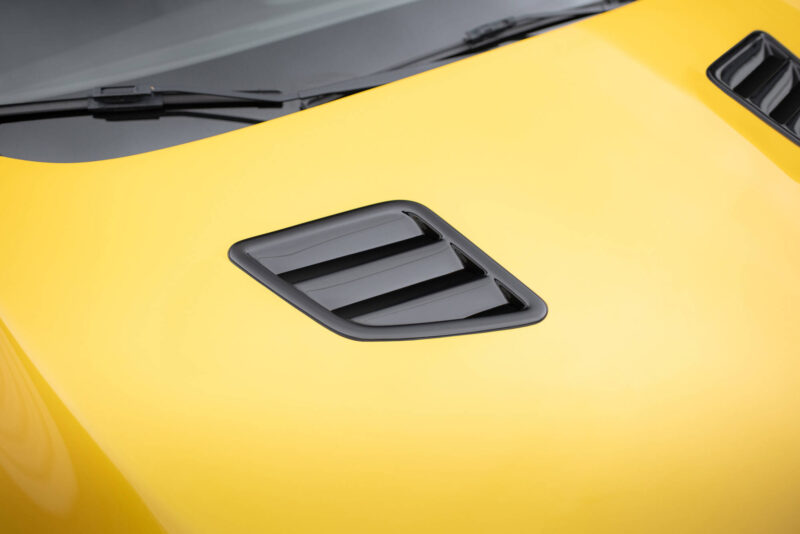 pol_po_Bonnet-Vents-459_6jpg - OPSHOLDERS Close-up of a bright yellow car hood with a black vent and nearby wiper blades visible on the windshield edge