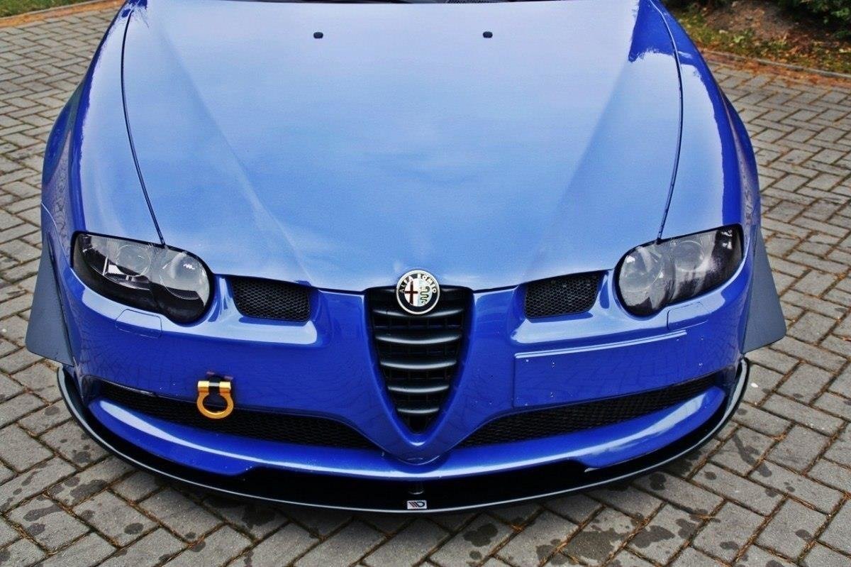 pol_po_FRONT-SPLITTER-suitable-for-Alfa-Romeo-147-GTA-621_2jpg - OPSHOLDERS Front view of a blue Alfa Romeo car on brick pavement, displaying the emblem, dual headlights, and yellow tow hook in the lower left corner.