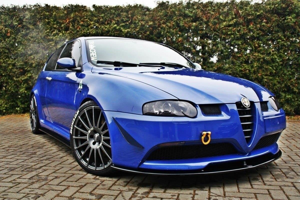pol_po_FRONT-SPLITTER-suitable-for-Alfa-Romeo-147-GTA-621_3jpg - OPSHOLDERS Blue Alfa Romeo sports car with lowered stance and large multi-spoke wheels parked on brick pavement, front tow hook visible.