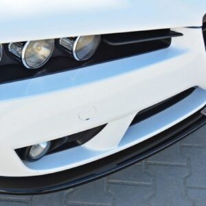 Front end of a white car with three round headlights and a black grille on a paved surface nearby.