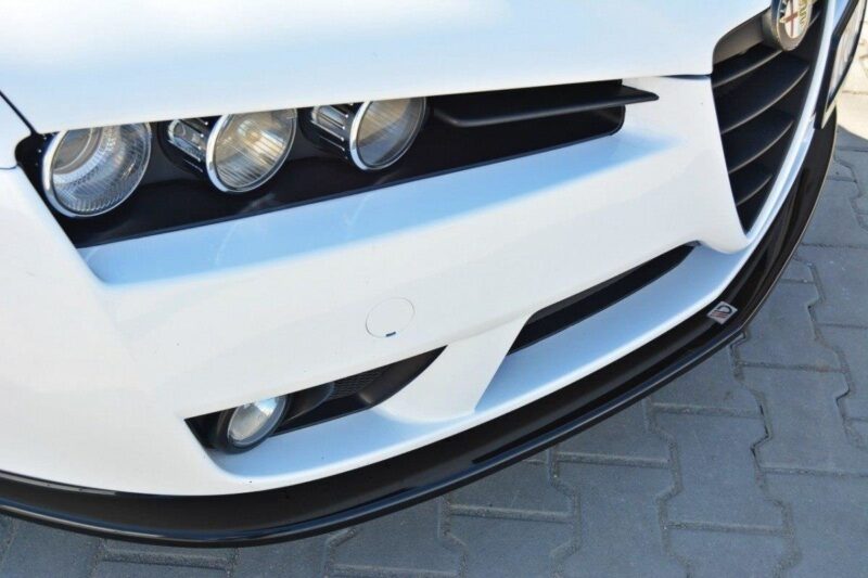 Front end of a white car with three round headlights and a black grille on a paved surface nearby.