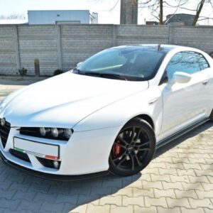 White sports coupe parked on a paved driveway, front-left angle, black multi-spoke wheels, red brake calipers, brick/stone fence in background.