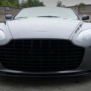Front view of a dark gray luxury sports car parked on a brick driveway with a tall stone wall in the background.