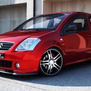 Red compact hatchback with large black alloy wheels parked near a concrete wall; built for style with a Maxton Design plate on the bumper.