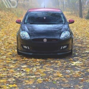 Front view of a black Fiat car with a red roof driving on a leaf-covered autumn road in a misty forest.