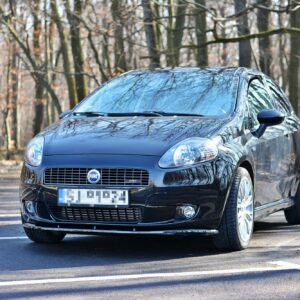 Front three-quarter view of a black Fiat car parked in a paved lot with bare trees in the background