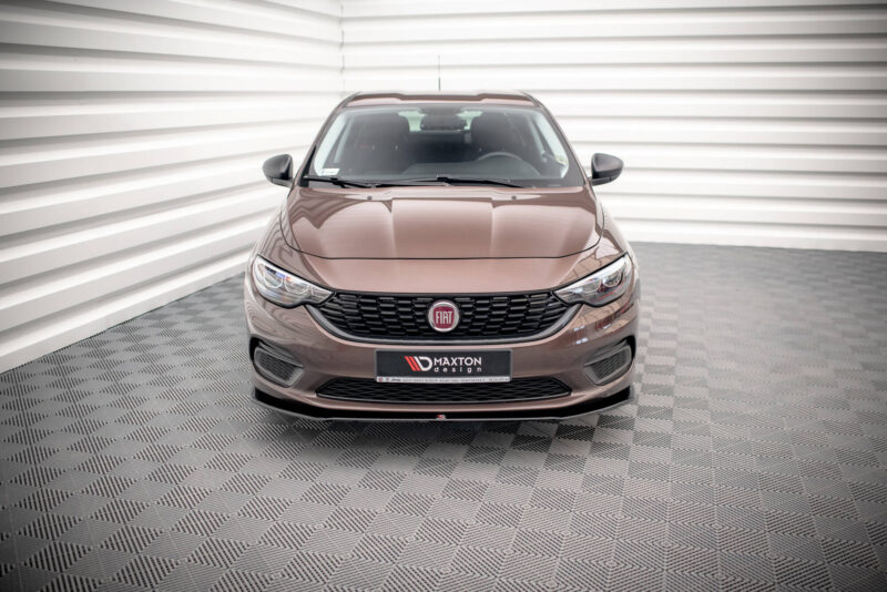 Front view of a brown Fiat SUV in a bright showroom with a checkered floor and white paneled walls, close to the camera showing the grille and emblem