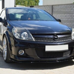 Front three-quarter view of a black Opel hatchback with custom bumper and large alloy wheels, parked on a paved driveway beside a white door and a concrete fence.