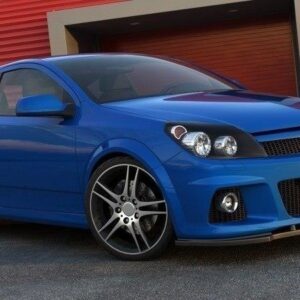 Blue Opel coupe with Maxton Design front bumper and splitter, parked in front of red storage units with large alloy wheels.