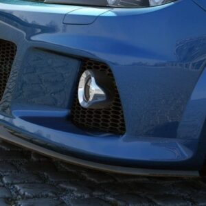 Close-up of a blue sports car's front end on a cobblestone street, featuring a large grille and fog light opening with a body kit.