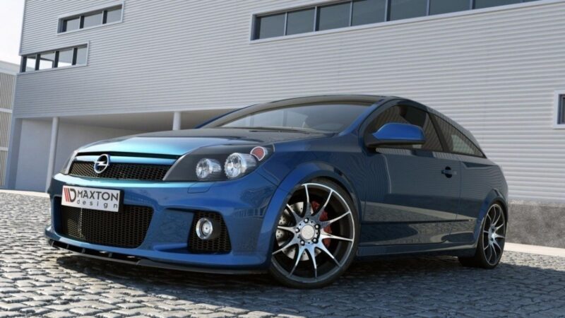 Blue sporty hatchback with large alloy wheels parked on cobblestone driveway in front of a modern industrial building; visible Brabus-style front bumper and grill details (Maxton design).