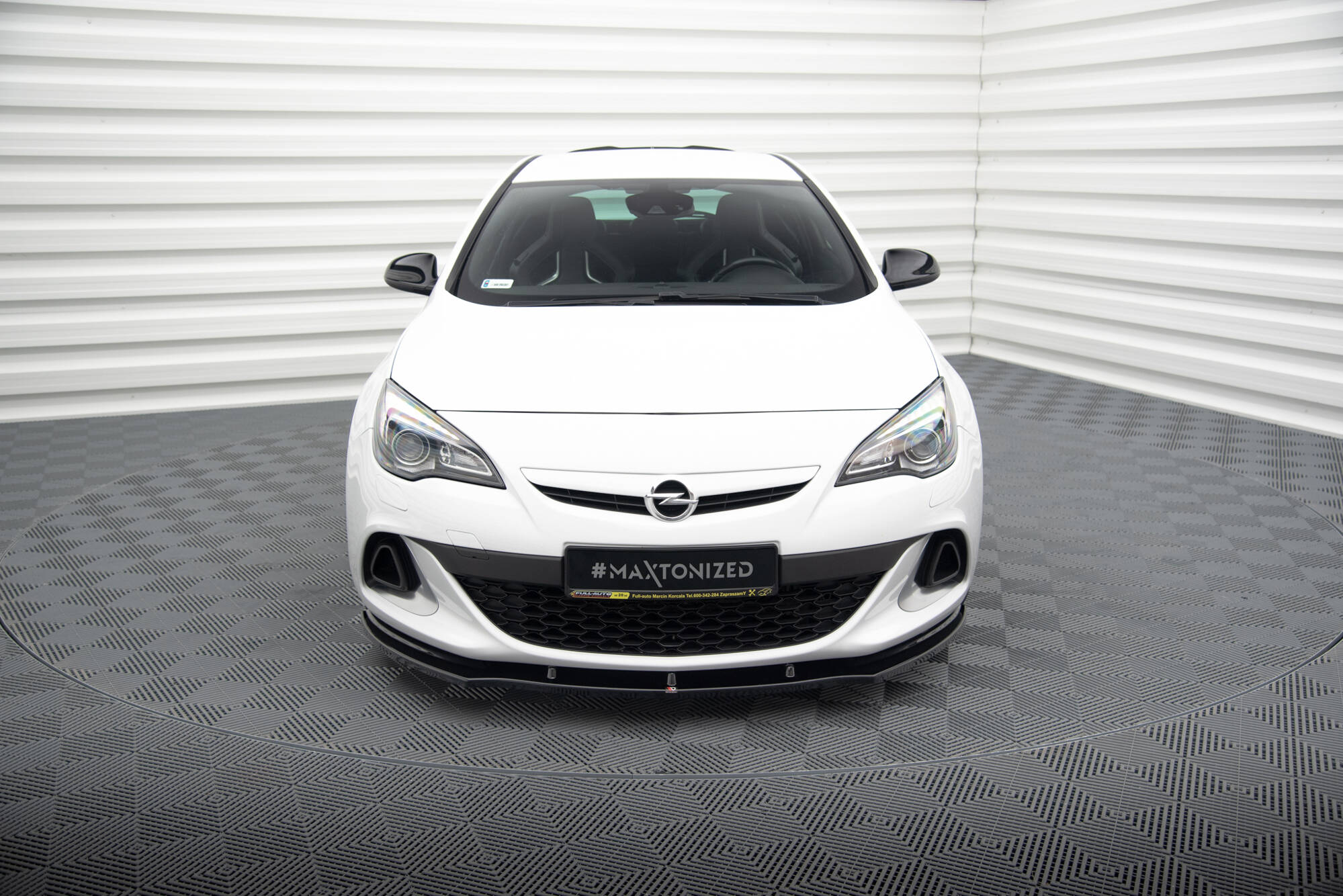 pol_po_FRONT-SPLITTER-suitable-for-Opel-ASTRA-J-OPC-VXR-v-1-837_2jpg - OPSHOLDERS Front view of a white Opel car in a studio with corrugated white walls; license plate reads #MAXTONIZED.