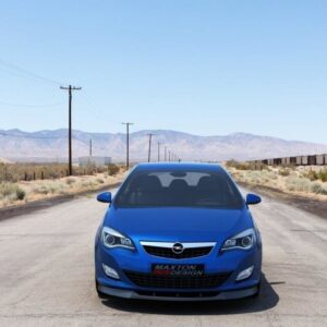 Front view of a blue sedan parked on a desert highway with mountains in the distance and a line of train cars to the right.