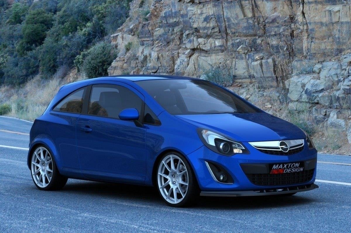 pol_po_FRONT-SPLITTER-suitable-for-Opel-CORSA-D-FACELIFT-843_1jpg - OPSHOLDERS Blue compact hatchback with aftermarket rims on a mountain road, rocky cliff in the background, conveying a sporty, customized look.